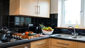 Una cocina moderna con baldosas negras, armarios de madera, una estufa a gas y un frutero sobre la encimera.
