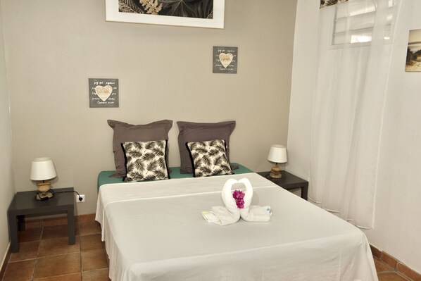 A neatly made bed with a heart-shaped towel arrangement, two patterned pillows, and a framed quote on the wall.