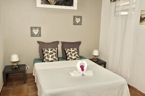 A neatly made bed with a heart-shaped towel arrangement, two patterned pillows, and a framed quote on the wall.
