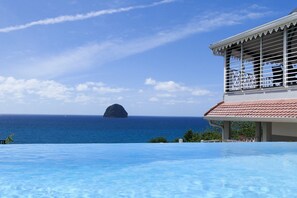 Una piscina infinita con vistas al océano y una isla distante.
