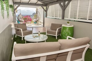 A covered outdoor seating area with a view of the sea, featuring a sofa, chairs, a table, and a green barrel. - 5-Bedroom Villa • Infinity Pool • 180° Ocean View (Le Diamant)