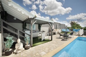 A poolside area with a covered outdoor kitchen, seating, and a Buddha statue. - 5-Bedroom Villa • Infinity Pool • 180° Ocean View (Le Diamant)