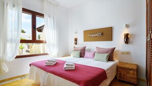 A neatly made bed with a red blanket, white linens, and two towels. There is a wooden headboard, a wall-mounted light, and a sign that reads "NAMASTE". - Casa La Goleta, Volcán y Mar (Playa Blanca)