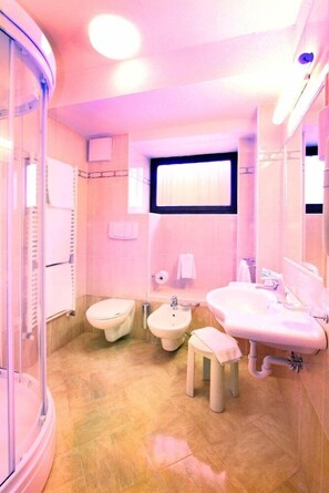 Un baño con cabina de ducha de vidrio, inodoro, bidé, lavamanos y un taburete pequeño.