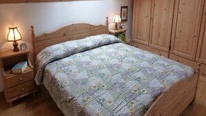 Ein Schlafzimmer mit einem Holz-Kopfteil, einem Bett mit blumigem Überwurf, einem Nachttisch mit Lampe und einem Kleiderschrank.