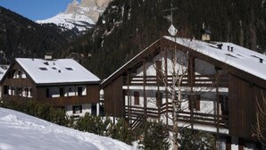 Eine Holzhütte mit Satteldach und Balkon, umgeben von verschneitem Gelände und einer Berglandschaft.