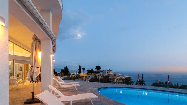 Zona de piscina con sillones de descanso y vista al mar.