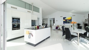 Una cocina moderna con electrodomésticos integrados, un comedor con mesa redonda y sillas, y una sala de estar con sofá y un cuadro grande.