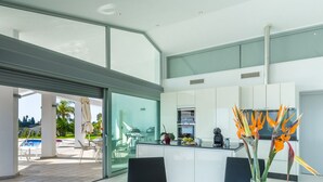 Una cocina moderna con una isla grande, un comedor con una pared de vidrio y vistas a un área de piscina exterior.