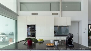 Una cocina moderna con armarios blancos, horno integrado, cafetera y un ventanal con vistas a la ciudad.