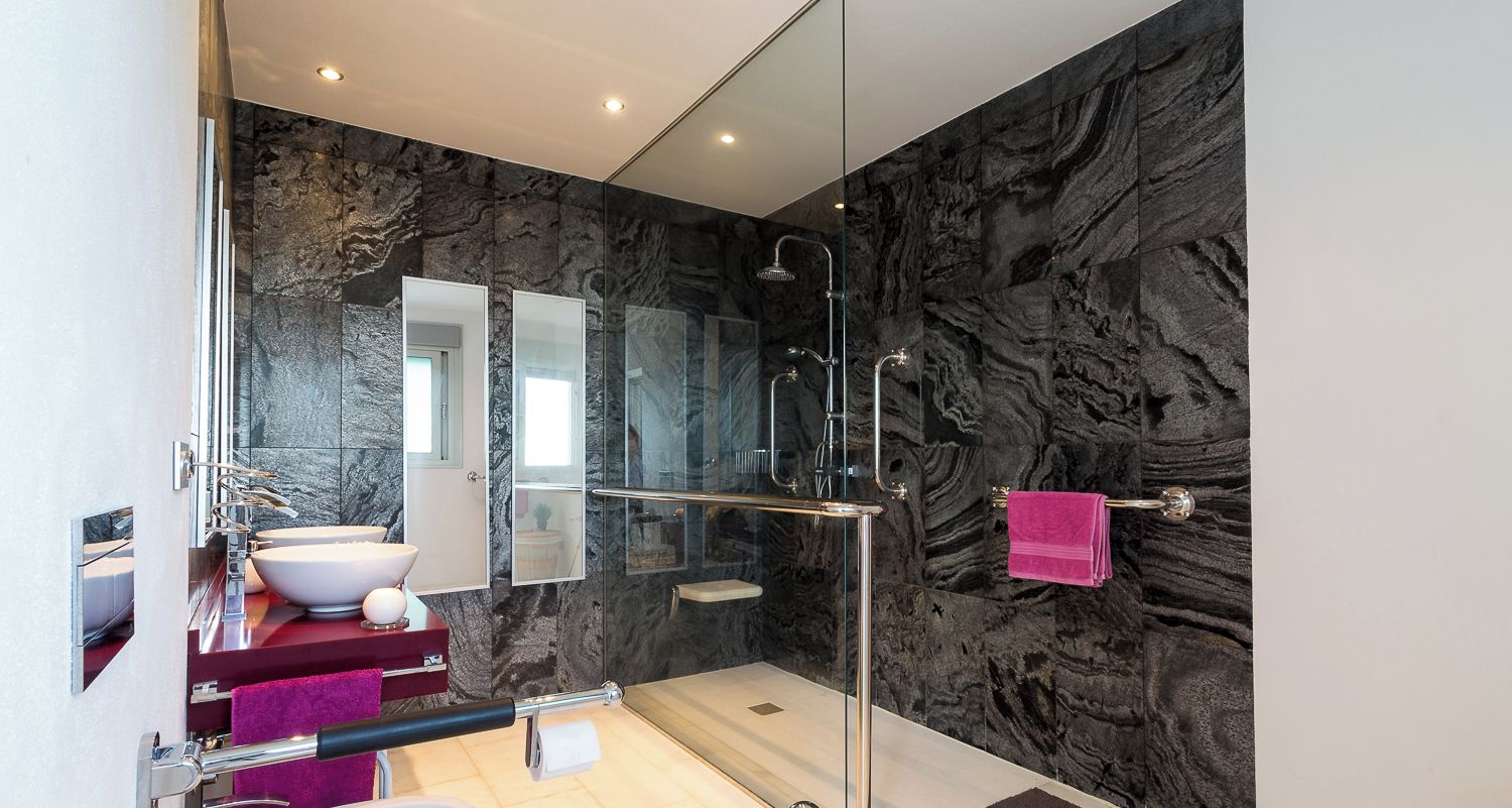 A modern bathroom with a glass shower enclosure, a white sink, and a marble backsplash.