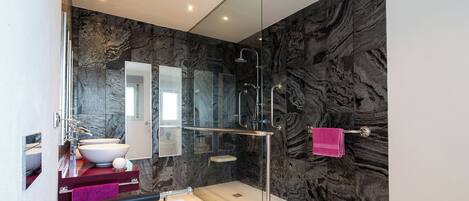 A modern bathroom with a glass shower enclosure, a white sink, and a marble backsplash.