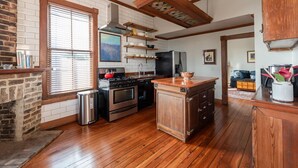 A kitchen with wooden floors, a brick wall, and a large window with blinds.
