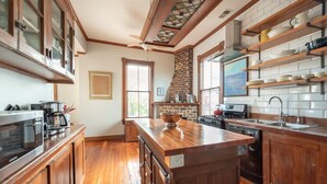 A kitchen with wooden cabinets, a central island, a brick stove, and a window with blinds.
