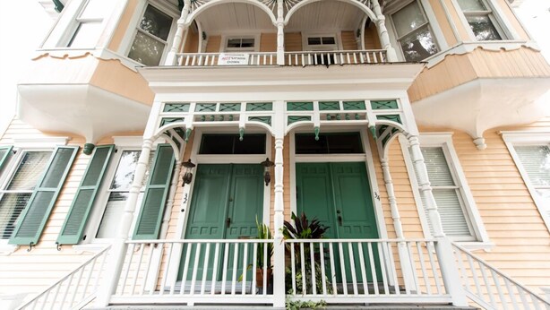 A multi-story building with a balcony, green shutters, and a sign indicating a ground floor restaurant.