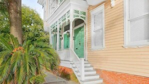 A two-story house with a porch, green doors, and a brick foundation.