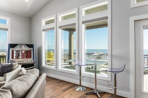 A living room with a couch, two bar stools, and large windows overlooking a balcony with outdoor furniture. - DEJA BLUE - Exquisite Beachfront - 5 Bedroom, sleeps 17, high end features! (Caplen)