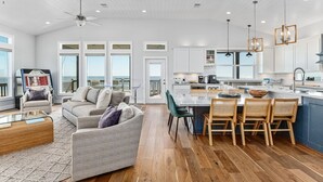 Een ruime woonkamer met een bank, een salontafel en een eethoek met stoelen, met een keuken op de achtergrond.