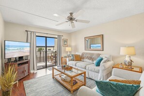 Una sala de estar con televisor, sofá, mesa de centro y un balcón con vista a la playa.