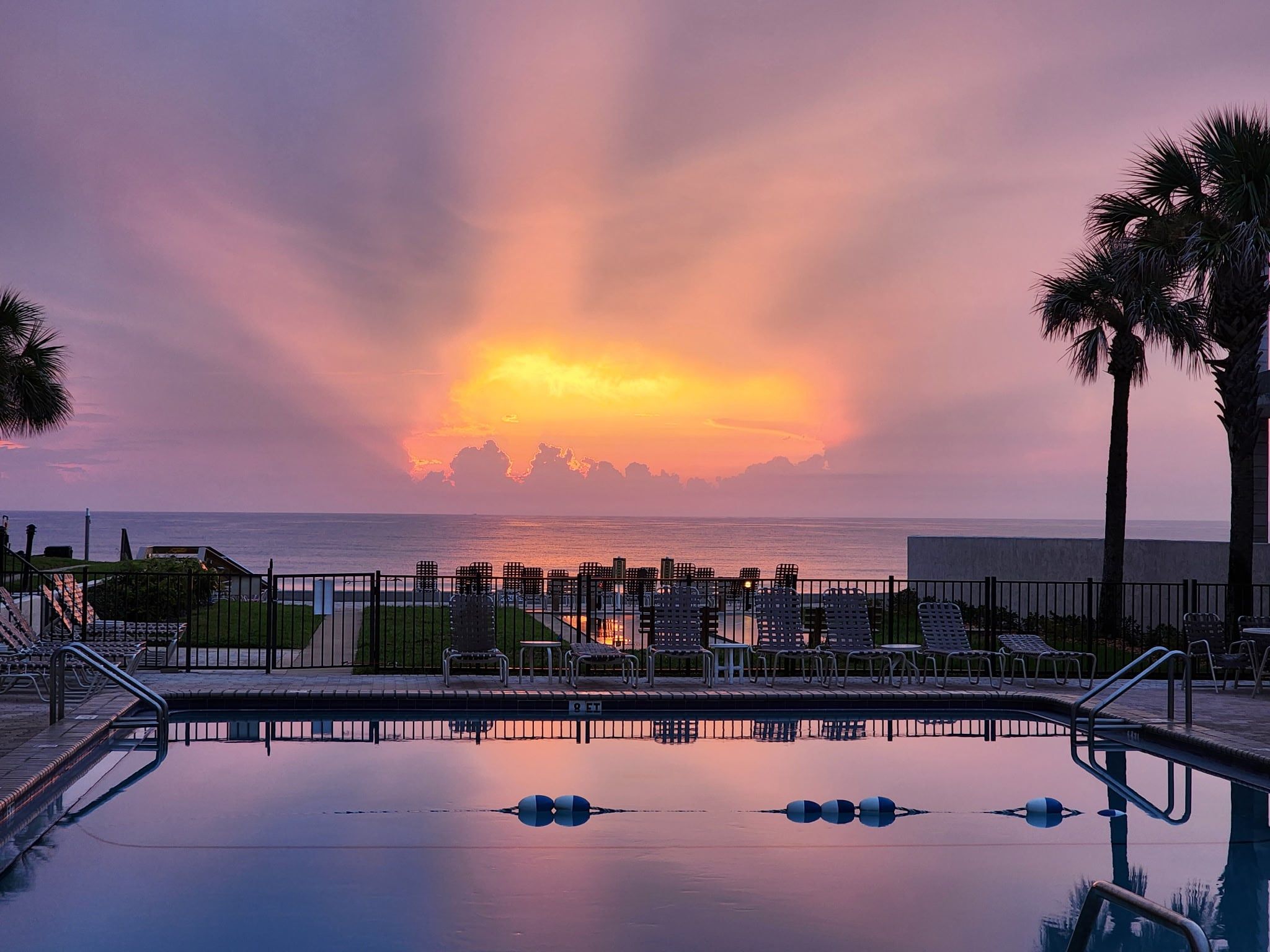 A swimming pool with lounge chairs and a view of the sunset over the ocean.