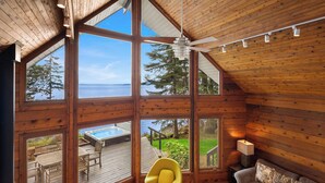 A spacious room with large windows, a ceiling fan, a yellow chair, a sofa, and a wooden coffee table. - Orcas Island, Aurora House #295 (Orcas Island)