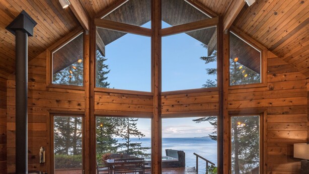 A cabin with a large central window, a fireplace, and a deck with a view of the water. - Orcas Island, Aurora House #295 (Orcas Island)
