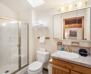 Une salle de bain avec une douche à parois de verre, des toilettes, un lavabo avec un meuble-vasque et un miroir orné d’un tableau encadré.