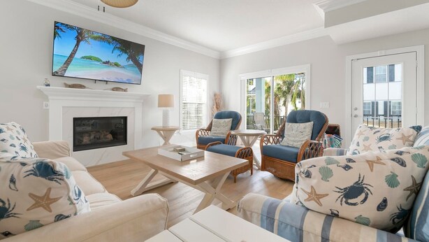 A living room with a fireplace, two blue armchairs, a sofa with starfish cushions, a television, and a ceiling fan. - ⚓ Heated pool, Hot Tub, Games & More, 5 min> walk to beach!⚓🐕🏖🌅 (Holmes Beach)