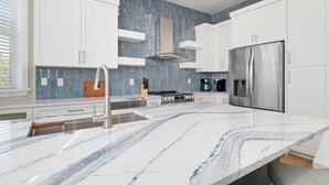 A modern kitchen with white cabinets, a stainless steel refrigerator, and a marble countertop. - ⚓ Heated pool, Hot Tub, Games & More, 5 min> walk to beach!⚓🐕🏖🌅 (Holmes Beach)