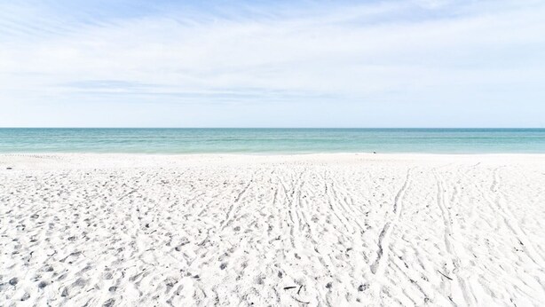 A wide sandy beach with footprints leading to the water. - Anna Maria Island Getaway (Holmes Beach)
