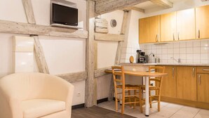 A cozy kitchen with exposed wooden beams, a dining table with chairs, and wooden cabinets.