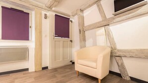 A room with exposed wooden beams, a cream-colored sofa, and a large window with purple blinds.