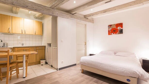 A bedroom with a bed, a small desk, and a kitchenette.