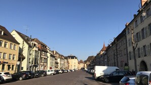 A cobblestone street lined with historic buildings, parked cars, and a white van.