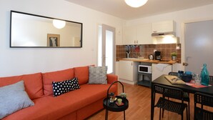 Un espace de vie compact comprenant un canapé, une table à manger avec des chaises, un coin cuisine avec un four à micro-ondes et un grand miroir.