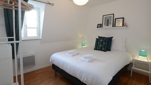 Une chambre à coucher bien rangée, avec un lit, deux lampes de chevet, une fenêtre avec des rideaux et une étagère murale ornée de tableaux encadrés.