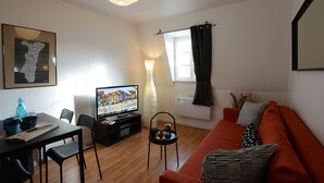 Un salon comprenant un téléviseur, un canapé, une table à manger avec des chaises et une fenêtre avec des rideaux.