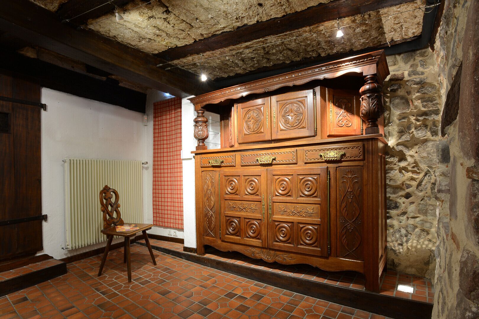 A room with a large wooden cabinet, a radiator, a checkered curtain, and a chair.
