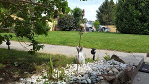 Un jardin avec un sentier, un petit étang orné d’une statue, et une pelouse avec une voiture garée au fond.