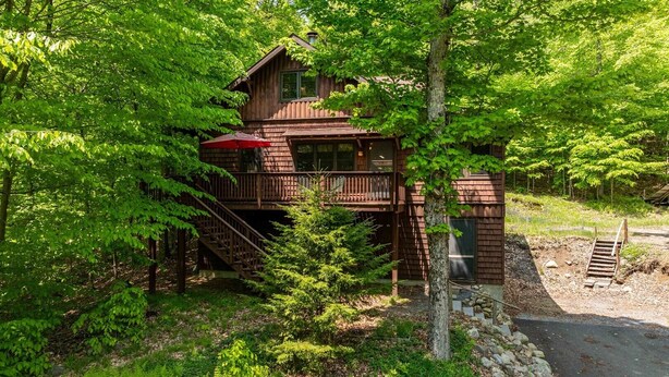 A wooden cabin with a balcony, surrounded by lush greenery.