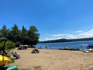 A lakeside beach with picnic tables, boats, and people. - Evergreen Lodge Old Forge (Old Forge)