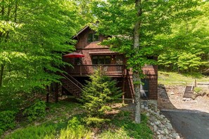 Eine Holzhütte mit Balkon und Treppe, umgeben von dichtem Grün.
