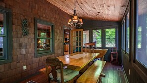 A wooden dining area with a large table, benches, and a chandelier.
