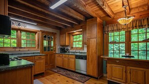 A rustic cabin-style kitchen with wooden cabinets, a built-in stove, and large windows offering a view of the forest.
