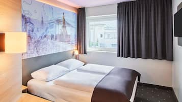 Een hotelkamer met een bed, een bureau, een lamp, een schilderij van een stadsgezicht, een raam met gordijnen, en een televisie aan de muur.
