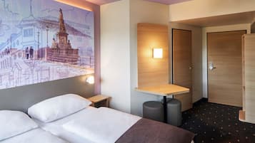 A hotel room with a bed, a small table, a wall-mounted light, and a door.