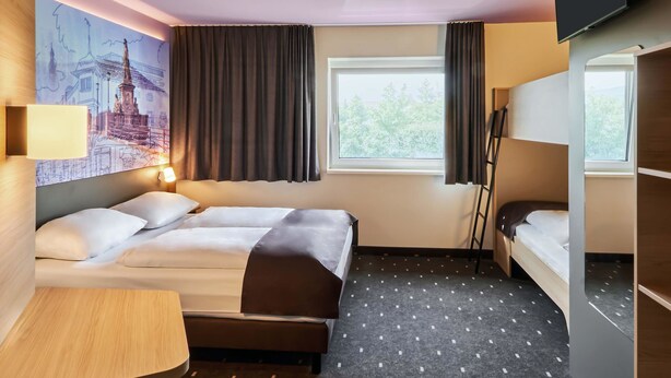 A hotel room with a bed, a desk, a chair, a TV, and a window with curtains. - B&B Hotel Heidelberg (Heidelberg)