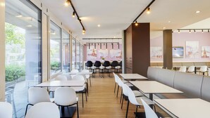 Un restaurante moderno con mesas y sillas blancas, ventanas amplias y obras de arte en las paredes.