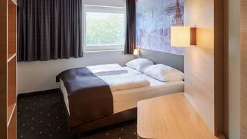 Een hotelkamer met een bed, een bureau, een raam met gordijnen en een muurschildering van een stadsgezicht.