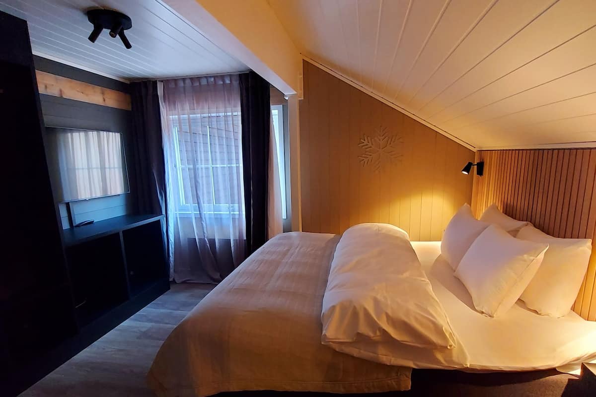A bedroom with a large bed, a wooden headboard, a bedside table, and a window with curtains.